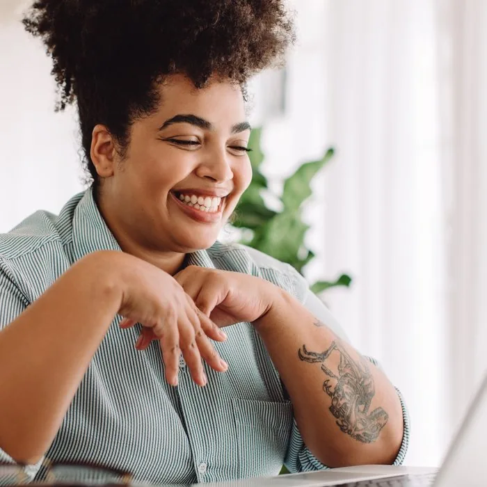A woman laughing while working on her laptop