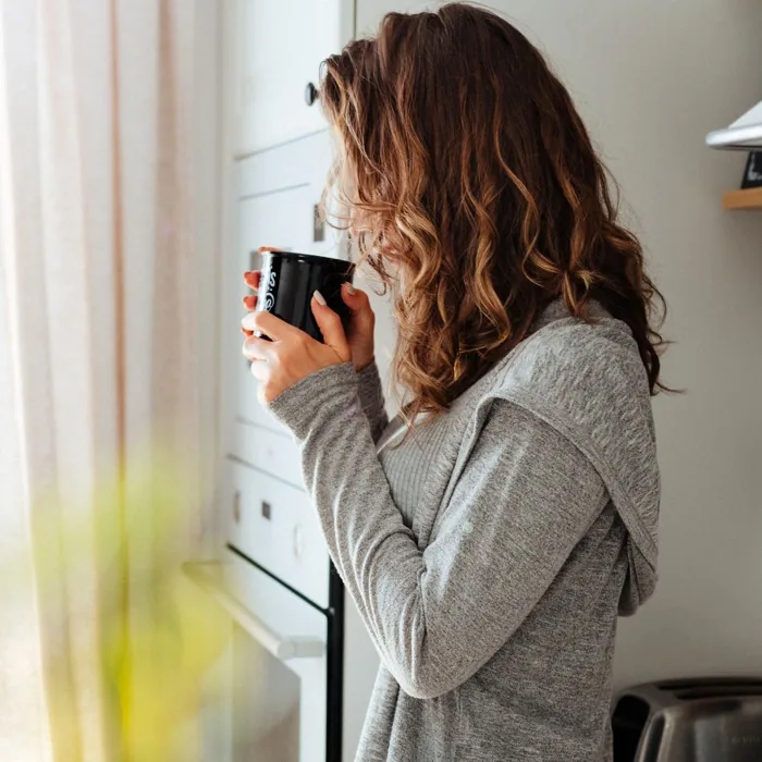 A woman drinking coffee by a kitchen window